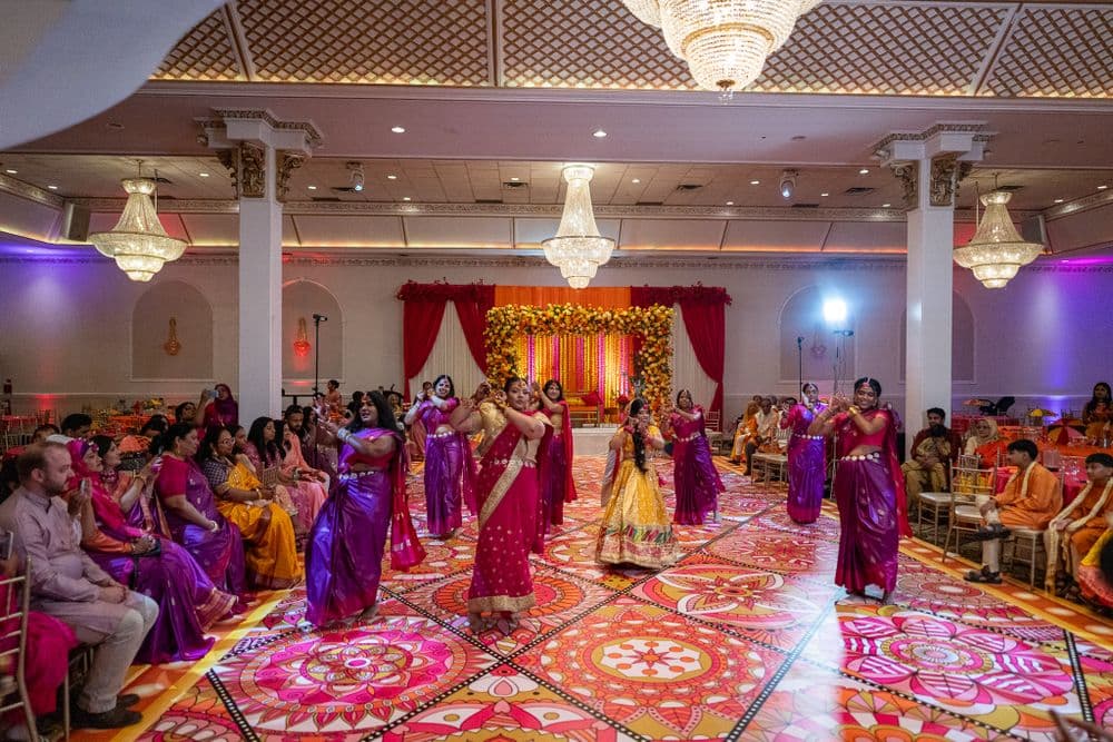 A wide reception hall scene with dancers performing in colourful outfits.
