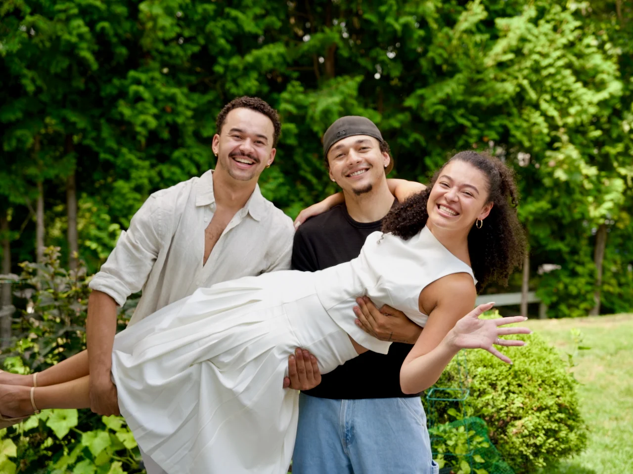 A man lifting and holding his partner as they both laugh together in a sunlit backyard.