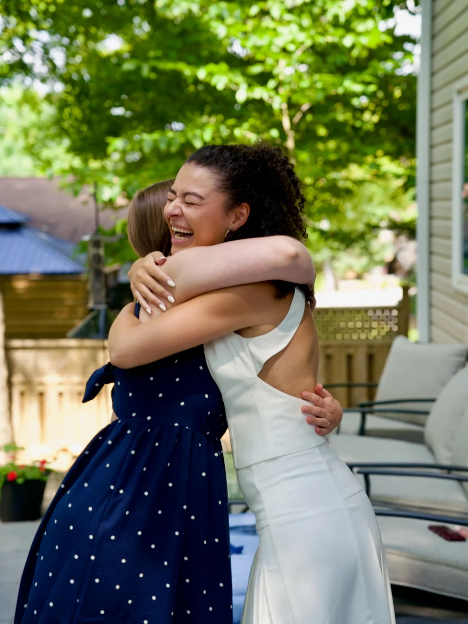 A couple embracing in a garden, the woman in a red dress laughing against her partner.