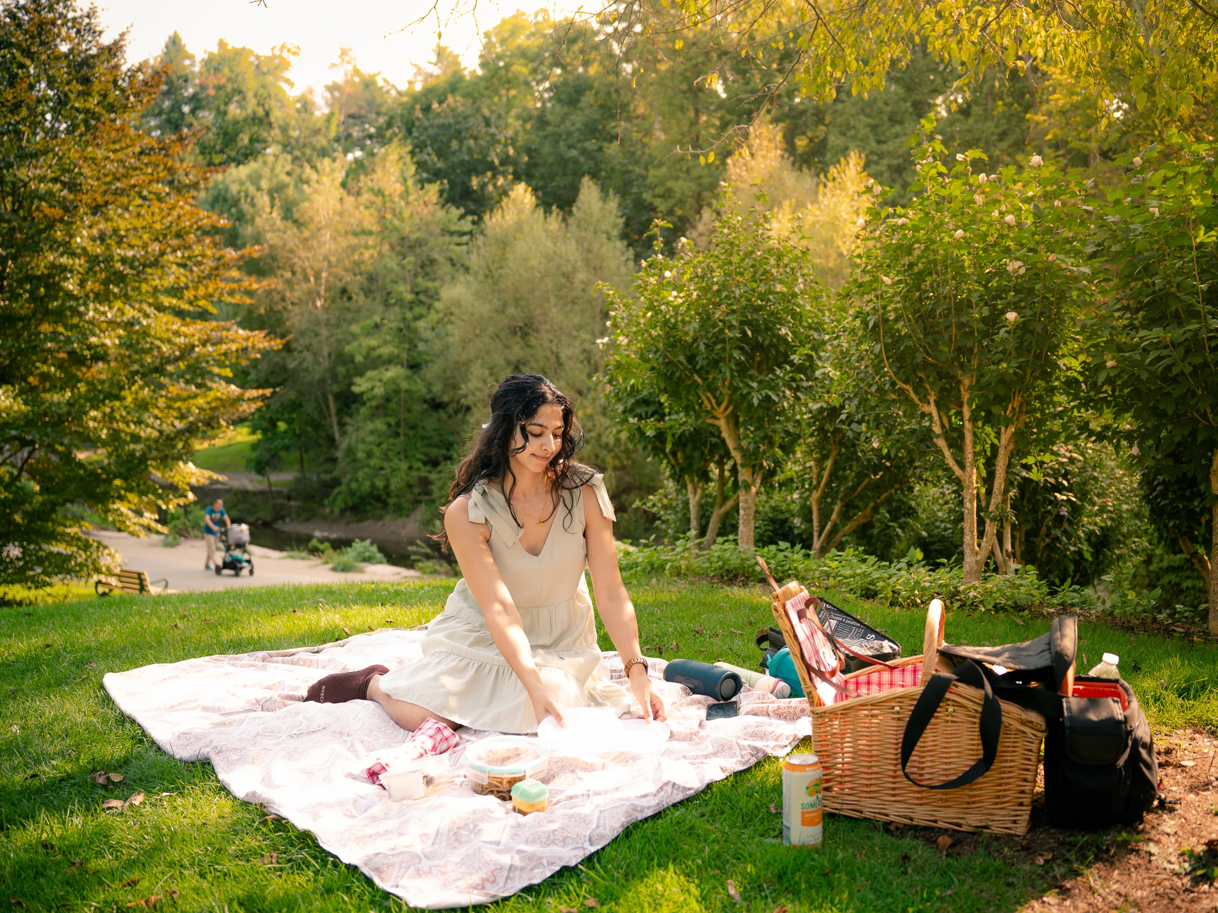 A woman arranging a picnic blanket in warm evening golden-hour park light.